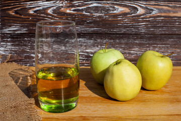 A glass of freshly squeezed apple juice and a green ripe apples on a table covered with a cloth...