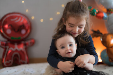 Two cute little sisters waiting for gifts from Santa Claus. Christmas decoration in the background with balloons and lights