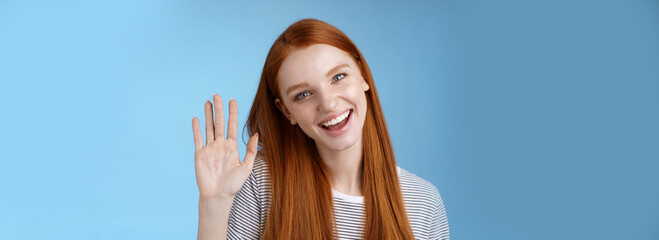 Obraz na płótnie Canvas Attractive confident redhead sassy girl pure clean skin blue eyes tilting head cheerfully waving hand hello hi gesture greeting you look camera friendly welcoming friend, standing studio background