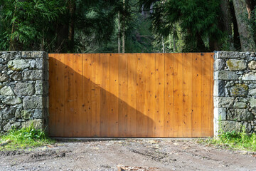 Wooden gates with remote control installed in high stone fence wall