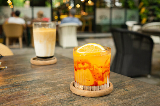 A glass of orange juice squash mixed with red strawberry syrup served with sunkist orange garnish put with blurred lamps tropical summer concept
