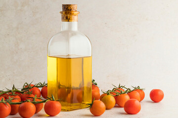 Glass bottle with extra virgin olive oil with some colorful cherry tomatoes on a light stone background.