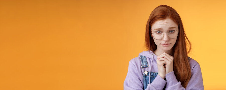 Silly guilty young shy redhead girlfriend asking forgiveness supplicating lower head look from under forehead frowning begging apology favour standing insecure sad pleading help, orange background