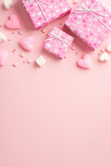 Valentine's Day concept. Top view vertical photo of present boxes in wrapping paper with heart pattern marshmallow candles and sprinkles on isolated pastel pink background with copyspace