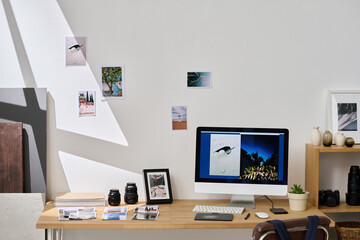 Horizontal image of modern workplace of photographer with computer monitor, photo cameras and fresh new photos