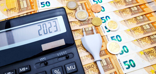 Calculator and electrical plug, in the background banknotes and coins. Concept of high cost of electricity, rising inflation and impending crisis in 2023