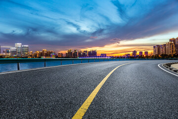 Asphalt road and city skyline with modern building at sunset in Suzhou, China.