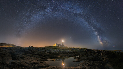 Beautiful landscape view of milky way arch over a lighthouse reflecting on water at night © Marcos