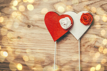 red and white heart on a stick on a wooden background. beautiful bokeh effect from a garland.