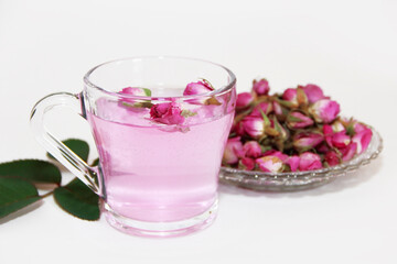 Pink tea in a transparent glass mug and small pink rose buds on a white background