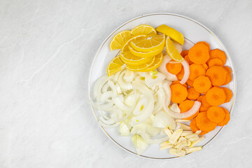 Sliced lemons, onions, garlic and carot on the plate ready for cooking