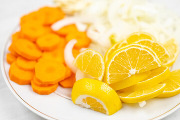 Sliced lemons, onions, garlic and carot on the plate ready for cooking