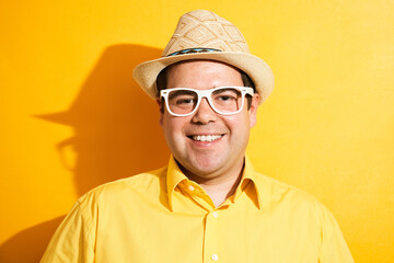 Portrait of positive fat man in hat kindly smiling isolated on yellow studio background, travel...