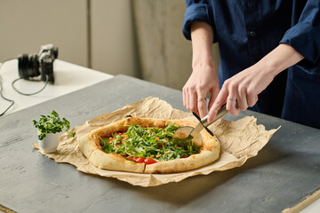 Close-up of female photographer cutting pizza with special knife for shooting of food blog