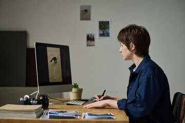 Young graphic designer retouching professional photos on computer monitor sitting at her workplace
