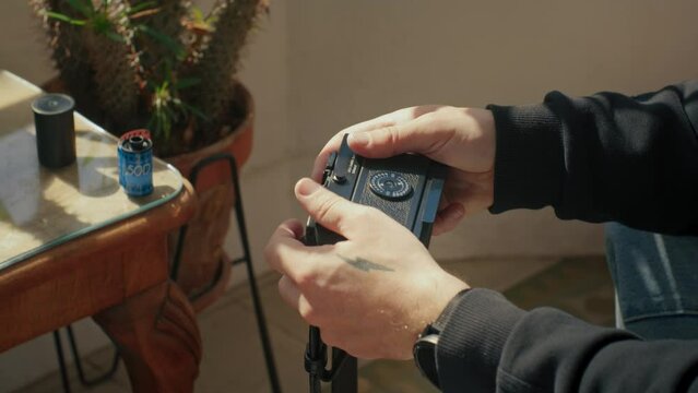 Handsome male hands putting a roll of film into retro camera. Photographer using camera to prepare it before shooting model in cosy sunny studio. Hobby, professional video about analogue photography