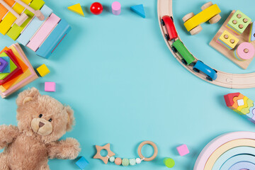 Baby kids toys frame background. Teddy bear, wooden educational stacking color recognition puzzle toys, wooden train and colorful blocks on light blue background. Top view, flat lay