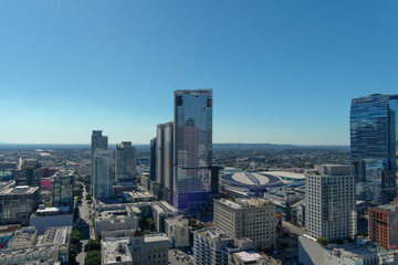 Fototapeta na wymiar aerial shot of the skyscrapers, office buildings and apartments in the city skyline with cars driving on the street and lush green trees with a clear blue sky in Los Angeles California USA