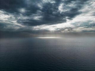 Obraz premium Aerial photo of a cloudy sky with sunbeams filtering and illuminating the surface of the calm sea of Palinuro. Photos of the Campania coast (southern Italy)