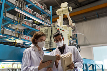 Two male and female researcher working with automatic agricultural technology with robotic arm system in indoor hydroponic vertical farm