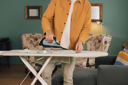Young man ironing a shirt at home in a living room