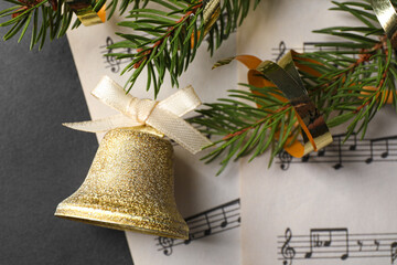 Golden shiny bell with white bow, fir branches and music sheets on grey table, top view. Christmas decoration