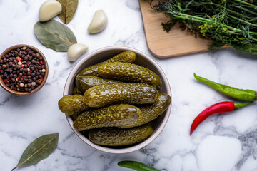 Bowl of pickled cucumbers and ingredients on white marble table, flat lay