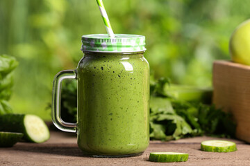 Mason jar of fresh green smoothie and ingredients on wooden table outdoors