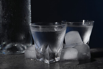 Vodka in shot glasses with ice on black table against dark background, closeup