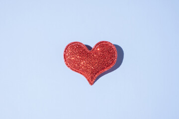Red glitter heart shape on blue background with hard shadow. Valentines day minimalistic symbol love
