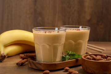 Tasty banana smoothie with almond and cinnamon on wooden table