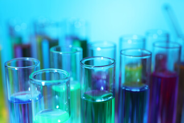 Many test tubes with colorful liquids on light blue background, closeup