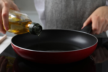 Woman pouring cooking oil from bottle into frying pan on stove, closeup