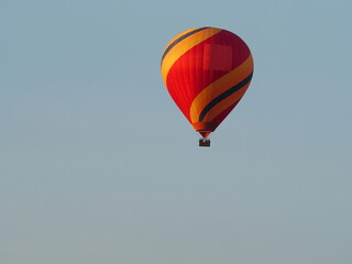 Hot air balloons with passengers flying over blue sky background. The balloons have a reddish yellow pattern. Tourists having fun and taking pictures
