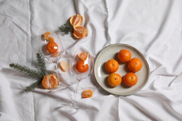 Delicious fresh ripe tangerines and glasses on white bedsheet, flat lay