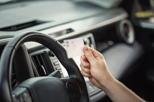 Close up person hand holding the driver license in front of the steering wheel