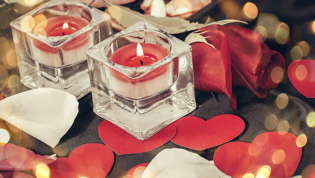 two candles and rose petals on a black silk background. Beautiful bokeh effect from a garland.
