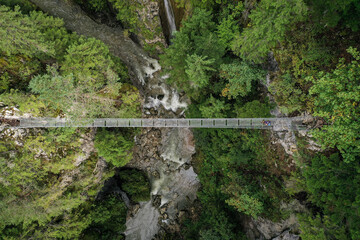 Fototapeta premium Drone photograph with hiker crossing a suspended metal bridge over a mountain gorge
