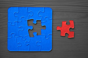 Puzzle piece on puzzle covered blue surface. wooden table background. One puzzle piece missing in an otherwise completed red jigsaw puzzle.