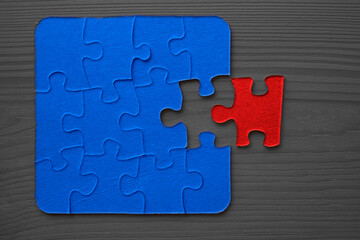 Mosaic from blue puzzles on a brown wooden background. 1 One red  puzzle was separated. One piece missing.