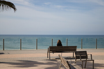 woman sitting on a bench looking at the horizon of the sea. The woman is relaxed and nostalgic looking at the sea. Concept relaxation and peace.