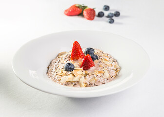 Oatmeal with almonds, blueberries and strawberries in a white plate on a white background