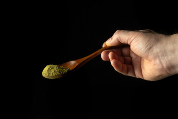 Mixture of dry ground herbs in a wooden spoon in a person hand before adding to tea. Free space for advertising on a black background.