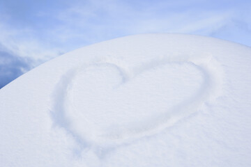 Fototapeta na wymiar A heart symbol painted on freshly fallen snow in a snowdrift, against a blue sky background. Soft focus.