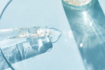 Serum gel texture swatch. Transparent drop with golden sparkles. Blue background. Face skincare...