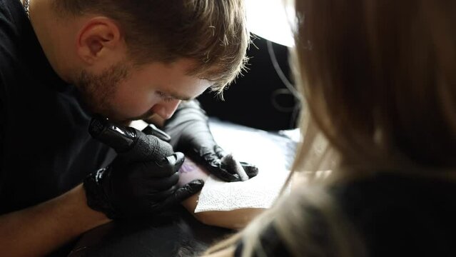 Tattoo master is tattooing a woman's hand. Wireless tattoo machine, safety and hygiene at work. Close-up of tattoo artist work. Tattoo salon