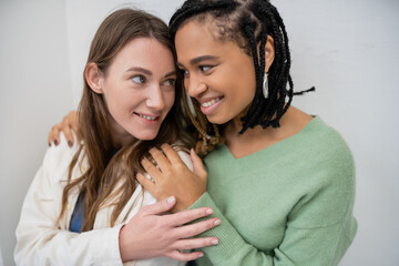happy interracial and lesbian women smiling while hugging each other.