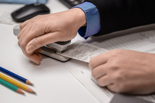 Woman accountant staples checks with a stapler at the office on the table