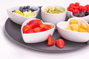 Assorted fresh berries and fruits in heart bowls on white background