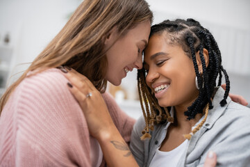 tattooed african american lesbian woman with engagement ring smiling and hugging happy girlfriend.